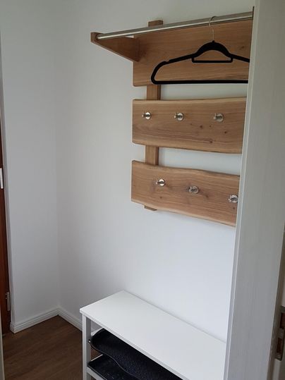 Ein kleiner Flur mit einem Holzkleiderständer und einer Bank. Die Wände sind weiß und der Boden ist holzfarben.