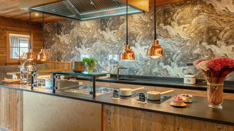 Eine moderne Küche mit eleganten Kupferlampen und einer stilvollen Wandgestaltung. Auf der Arbeitsfläche sind verschiedene Zutaten und Utensilien ordentlich platziert.