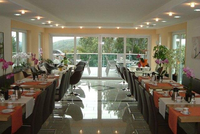 Ein helles Restaurant mit modernen Möbeln und eleganten Tischen. Große Fenster bieten einen Blick auf die Natur und lassen viel Licht hereinkommen.