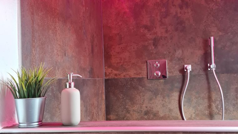 Een moderne badkamer met houten betimmering en een warme verlichting in roze. Op de voorgrond staan een plant en een zeepdispenser.