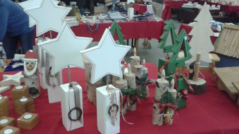 Eine Verkaufsfläche mit handgemachten Weihnachtsdekorationen. Zu sehen sind Sterne, Tannenbäume und verschiedene kleine Figuren auf einem roten Tisch.