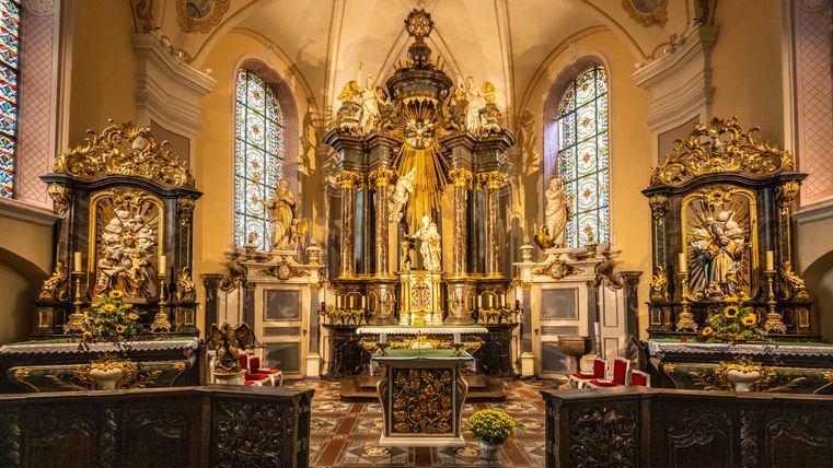An impressive church with an artistically designed altar and large windows. The golden decoration and sculptures give the space a ceremonial atmosphere.