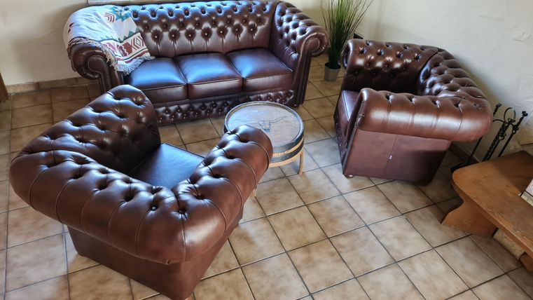 Een gezellige woonkamer met een donkerbruin leren bankstel en een kleine tafel. De inrichting is klassiek en uitnodigend.