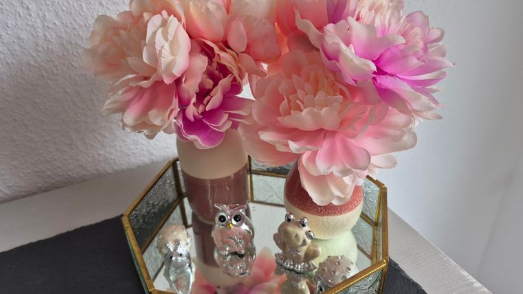 A decorative container with artificial flowers in soft shades of pink and cream. Inside, there are also small figures in the shape of owls and other animals.