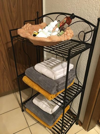 A black shelving system with multiple levels. At the top is a bowl with care products, and below are folded towels in various colors.