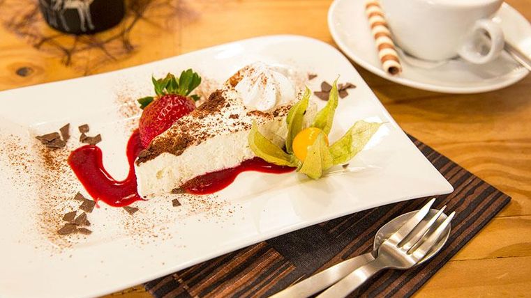 A delicious dessert with cream, strawberries, and chocolate sauce on a white plate. Next to it is a cup of coffee on a table.