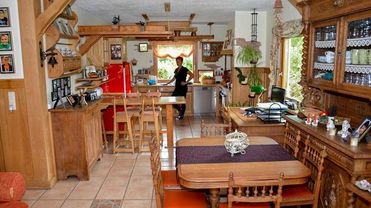 A rustic kitchen with wood decor and a large dining table. In the background, there is a person working in the kitchen.