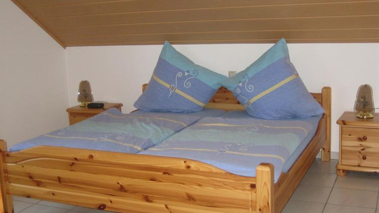 Une chambre confortable avec un lit en bois et de grands coussins bleus. À côté du lit, il y a deux tables de nuit.