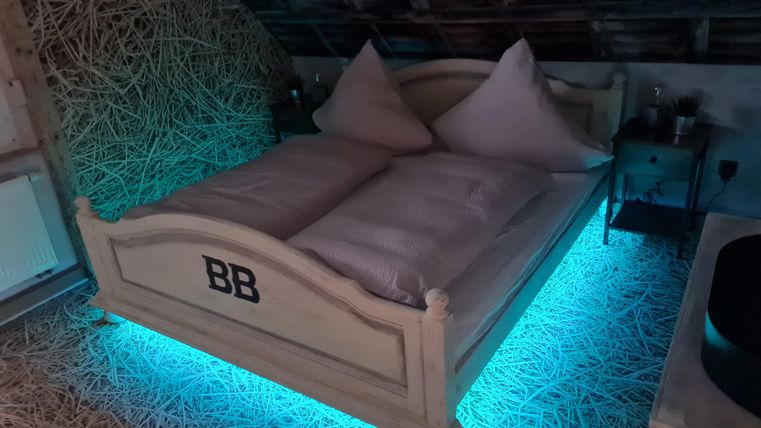 Een modern bed met blauwe LED-verlichting. De ruimte heeft een gezellige, rustieke sfeer met houten details.