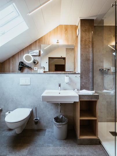 Een moderne badkamer met douche, wastafel en toilet. De ruimte heeft lichte muren en een groot raam dat daglicht binnenlaat.