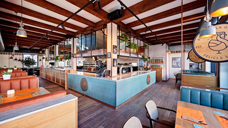 A modern restaurant with wooden ceilings and cozy furnishings. The atmosphere is inviting and bright, with open kitchen areas.