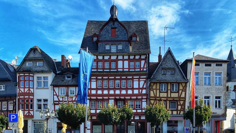 Fachwerkhäuser am Marktplatz in Adenau mit blauen Himmel und Flaggen.