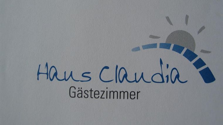 A sign with the inscription "House Claudia" and a reference to "Guest Room". The design features a stylized sun and a colored arc line.