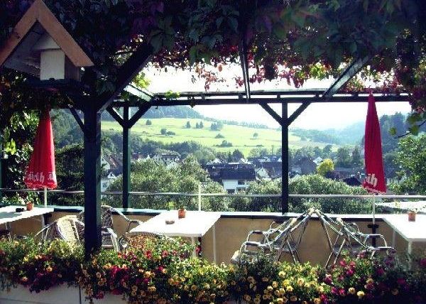 Une belle terrasse avec des suspensions de fleurs et une vue sur le paysage verdoyant. Des parasols rouges créent une atmosphère accueillante.