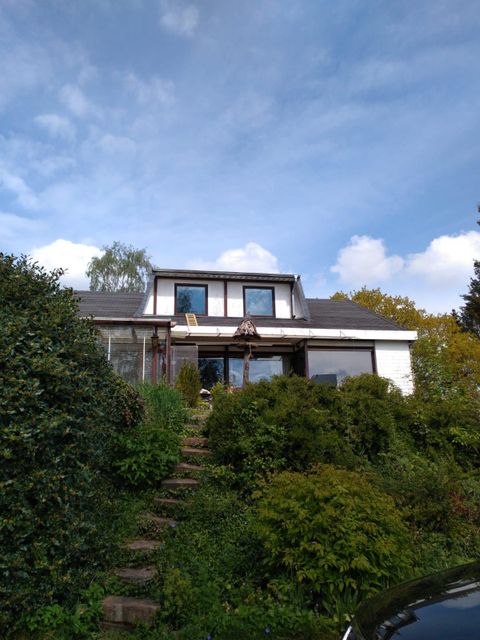 A charming house surrounded by lush greenery and shrubs. The sky is clear, making the day look friendly.