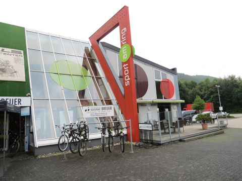 Ein modernes Sportgeschäft mit großen Fenstern und bunten Akzenten. Vor dem Eingang sind mehrere Fahrräder abgestellt.