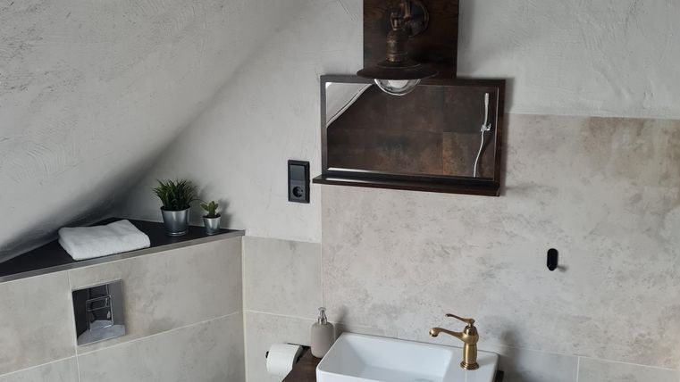 Een moderne badkamer met een houten commode en een wastafel. De muren zijn licht en het plafond heeft een rustiek houten uiterlijk.