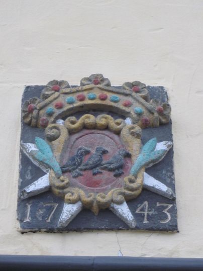 Ein historisches Wappen mit zwei Vögeln und einer dekorativen Krone. Das Jahr 1743 ist ebenfalls dargestellt.