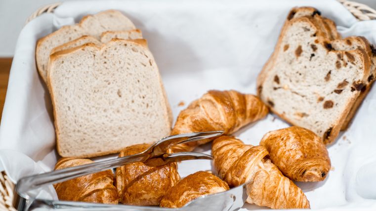 Een mand met verschillende soorten brood, waaronder sneetjes toastbrood en croissants. Het brood is netjes gerangschikt en nodigt uit tot een ontbijt.