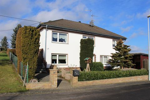 A modern, two-story residential house with a green garden and well-maintained hedges. The sky is clear and blue, creating a pleasant atmosphere.