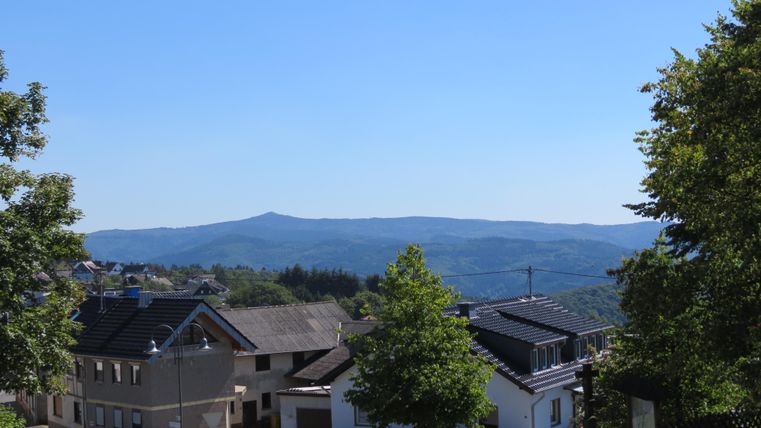 Ein malerisches Dorf in der Natur mit Häusern und Bäumen. Im Hintergrund sind sanfte Hügel unter einem klaren blauen Himmel zu sehen.