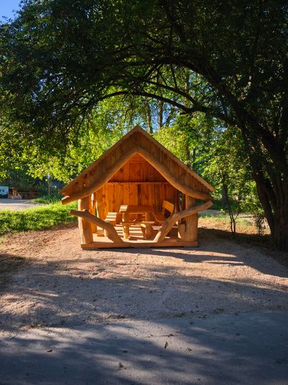 Ein gemütliches Holzhaus steht unter den Bäumen. Der klare Himmel und die grüne Umgebung schaffen eine einladende Atmosphäre.