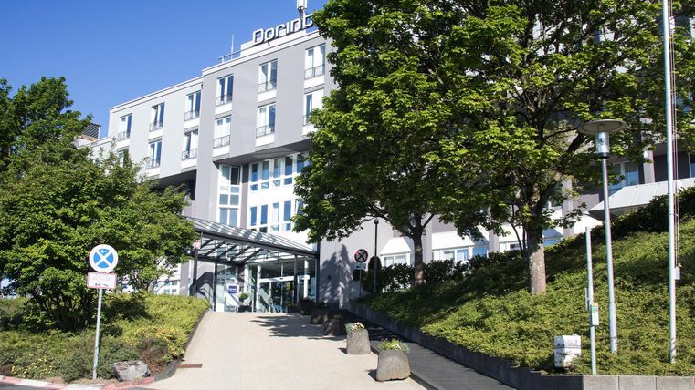 A modern building with clean lines and large windows. In the foreground, there are trees and a well-maintained environment.