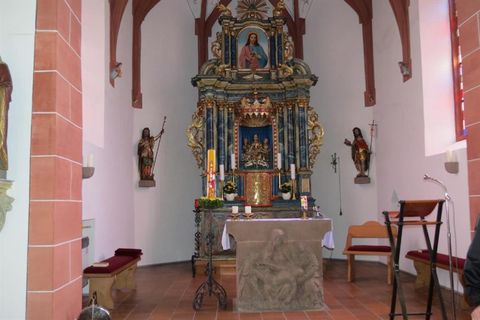 Ein schöner Altar in einer Kirche mit kunstvollen Verzierungen. Auf der linken Seite stehen religiöse Statuen und es gibt Sitzbänke im Raum.