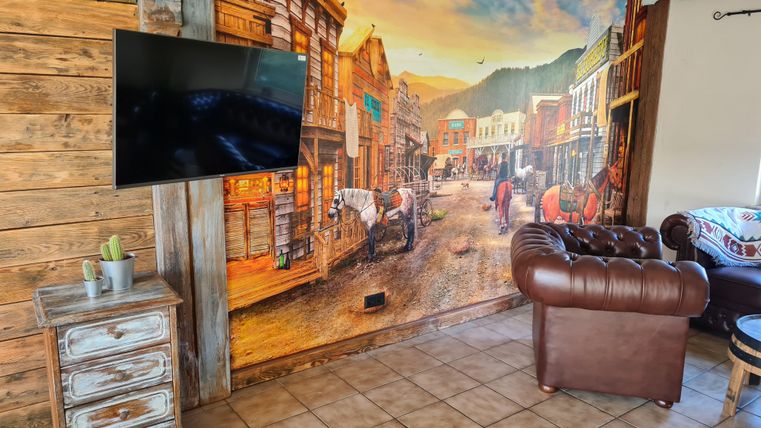 Een gezellige kamer met een grote muurschildering van een historische stadsstraat. In de kamer staan een televisie en een comfortabele leren bank.