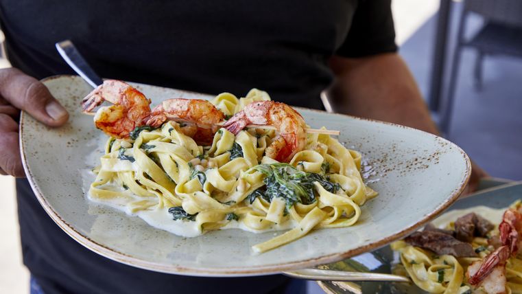 Ein Teller mit frischen Fettuccine und Garnelen, garniert mit Spinat. Das Gericht wird von einer Person serviert.