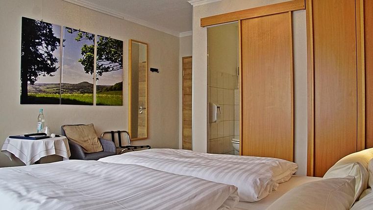 Une chambre cozy avec deux lits et une chaise. Un grand tableau d'un paysage est accroché au mur.