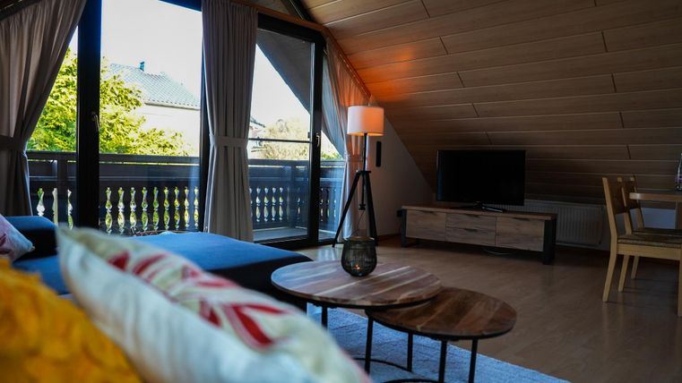 Een moderne woonkamer met schuine wanden en grote ramen. De ruimte is gezellig en licht, met uitzicht op de natuur buiten.