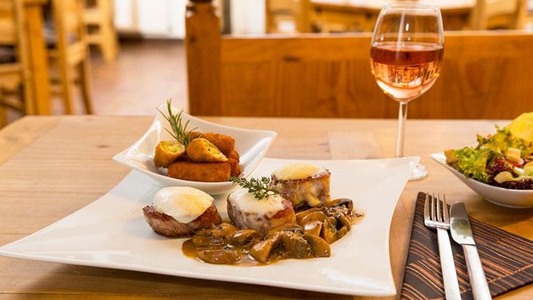 A beautiful plate with delicious meat, mushrooms, and a side dish. Accompanied by a glass of rosé wine and a fresh salad.