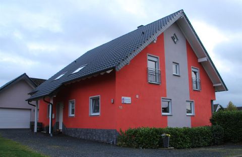 A modern house with a red and gray facade. It has a slanted roof and windows that let light in.