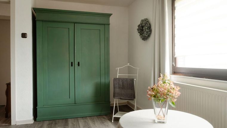 Ein gemütlicher Raum mit einem grünen Kleiderschrank und einem kleinen Tisch. Auf dem Tisch steht eine Vase mit Blumen, und ein bequemer Stuhl ist in der Ecke.