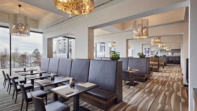 A modern restaurant with elegant tables and cozy seating. The large windows offer a beautiful view and plenty of natural light.