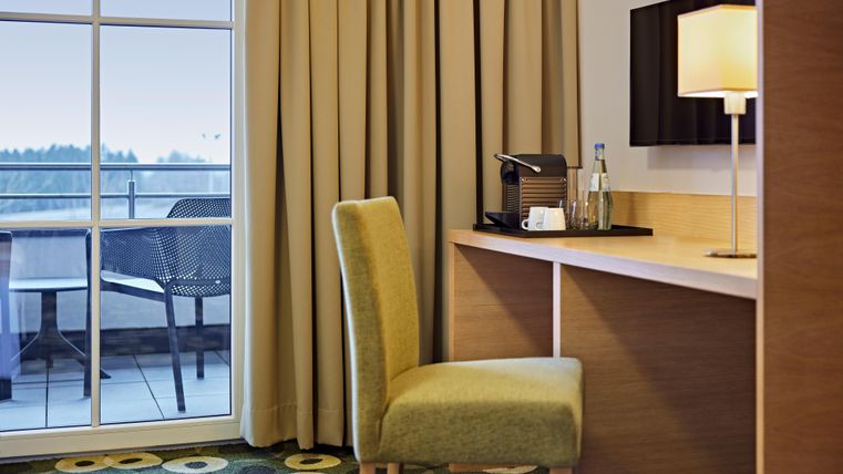 A modern room with a desk and a comfortable chair. The room has large windows and a balcony with a view.