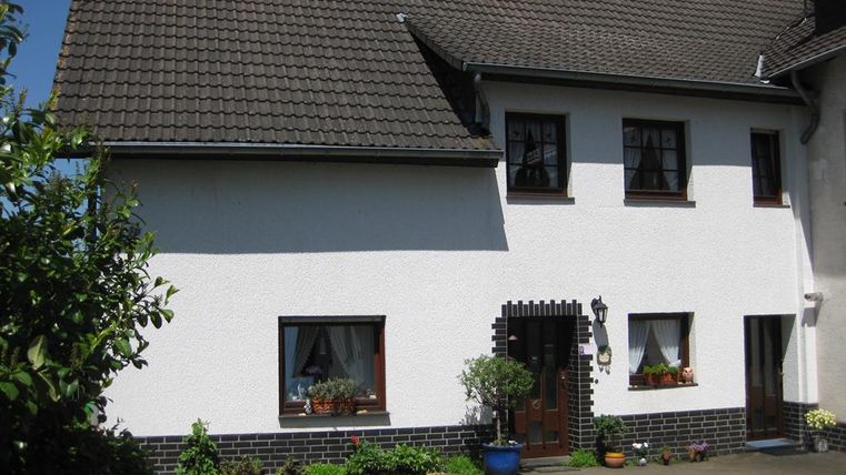 Ein schönes Haus mit einem weißen Außenanstrich und einem schiefergrauen Dach. Vor dem Eingang stehen mehrere Pflanzen in Töpfen.