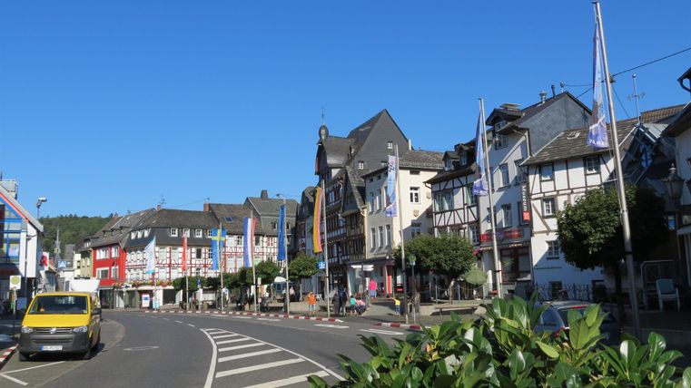 Une rue de ville pittoresque avec de beaux bâtiments et des arbres ombrageants. Le ciel est bleu et l'atmosphère est vivante.