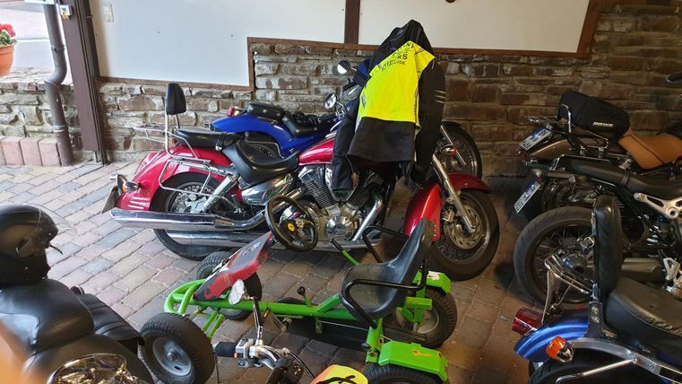 Een verzameling motorfietsen staat in een garage. In het midden staat een groene speelgoedauto.