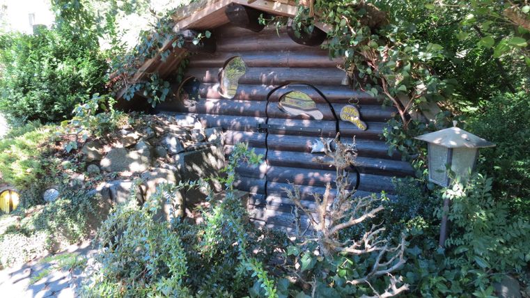 Ein kleines, verstecktes Holzhaus umgeben von üppigem Grün und Pflanzen. Es strahlt eine gemütliche und einladende Atmosphäre aus.