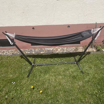 A black hammock is set up on green grass. In the background, a light wall is visible.