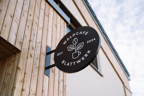 Ein Schild des Waldcafés "Blattwerk" mit einem modernen Design. Das Café ist im Jahr 2024 gegründet worden und zeigt eine natürliche, einladende Atmosphäre.