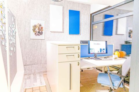 Un bureau moderne avec un bureau, deux écrans et un meuble à tiroirs. Les murs sont décorés avec des accents bleus et des œuvres d'art.