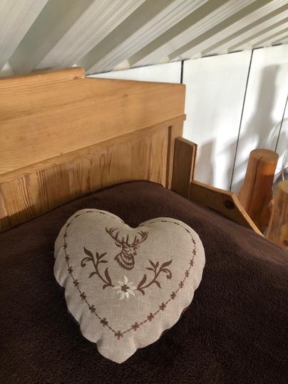 A heart-shaped cushion with a deer appliqué on a bed. The cover is light with a floral pattern.