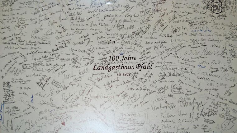 Een verzameling handtekeningen en berichten op een muur ter viering van het 100-jarig bestaan van Landgasthaus Pfahl. De vele persoonlijke boodschappen getuigen van herinneringen en dankbaarheid.