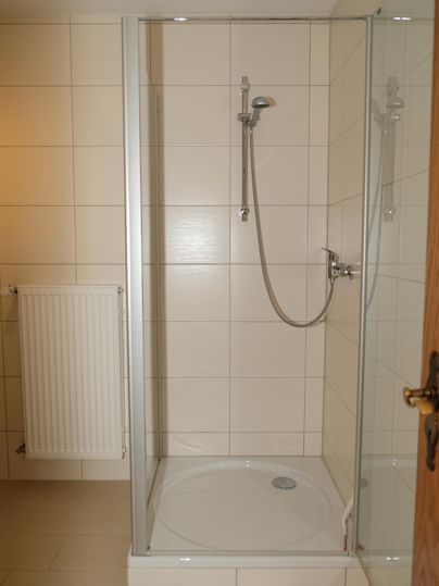 Une douche moderne avec une paroi en verre dans une salle de bains lumineuse. Les murs sont équipés de carrelage blanc et il y a un porte-serviettes.
