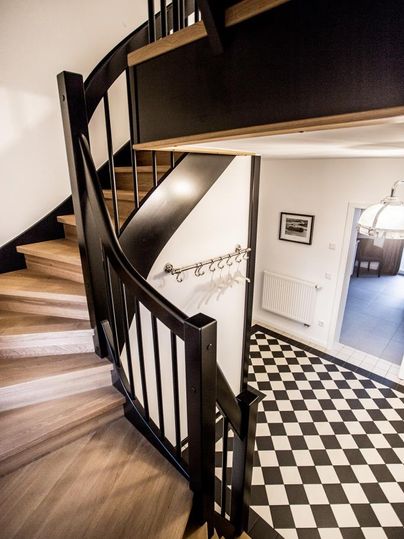 Eine elegante Wendeltreppe mit Holzstufen führt zu einem modernen Flur. Der Boden ist mit einem stilvollen Schachbrettmuster in Schwarz und Weiß gestaltet.