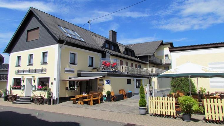An inviting inn with a large outdoor area. There are tables and chairs on the terrace as well as sun umbrellas.