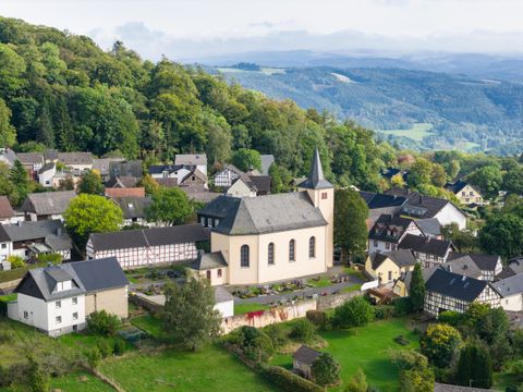 Un village pittoresque avec une église et des maisons traditionnelles. Entouré de collines vertes et d'arbres.